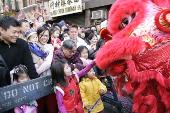 People behind a barrier in Chinatown during a Lunar New Year celebration and dragon character comes to see the children.
